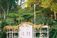 a refined and chic wedding drink bar of open shelving units and a stand with various kinds of beer, with greenery and blooms and a bold fall leaf garland