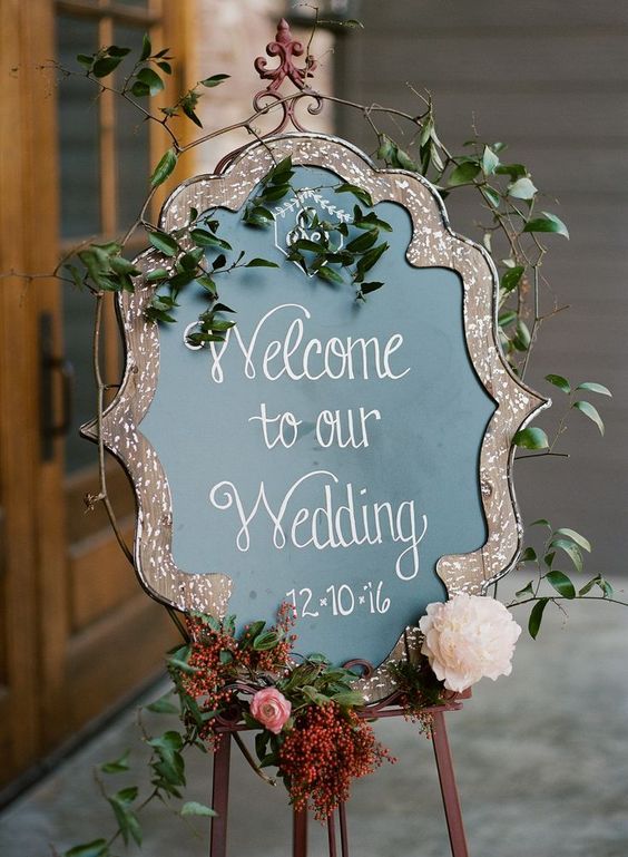 a refined chalkboard sign accented with a lovely splatter cutout frame, with greenery and some blooms is a lovely idea for a wedding