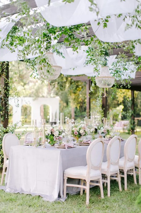 a refined garden wedding reception with lilac and pink linens, beaded chandeliers and greenery climbing, neutral and pink blooms