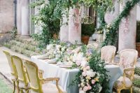 a refined garden wedding tablescape with a lush greenery and pastel bloom runner, pastel plates and linens and refined chairs