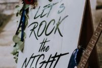a rock n roll sign decorated with greenery and blooms and with a guitar next to it is a very original decoration