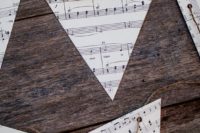 a rustic banner made of note paper triangles on twine is a simple and cool idea for a music-inspired wedding