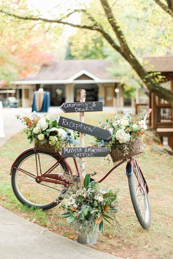 a rustic bike with baskets filled with neutral blooms, foliage and greenery, chalkboard signs is a cool idea for a wedding