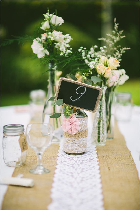 a rustic cluster wedding centerpiece of bottles and jars, with burlap, lace, blooms and a chalkboard sign is amazing