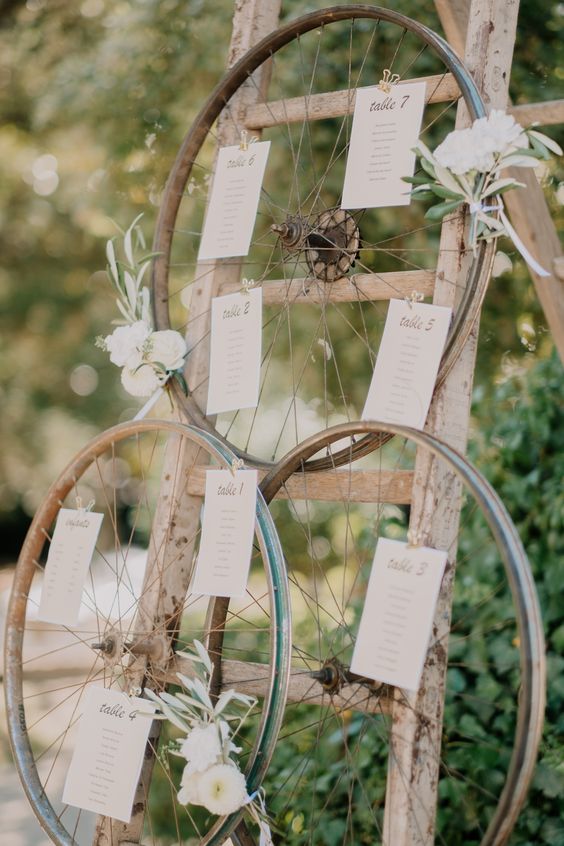 a rustic seating plan of a ladder, old metal wheels with blooms and the seating plan is a cool idea for a wedding