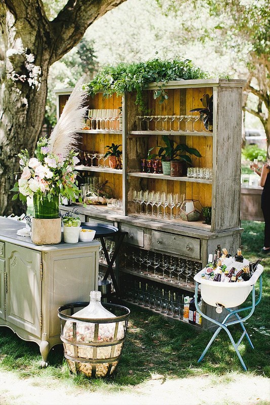 a rustic wedding drink bar of a relcaimed wood vintage buffet, greenery, blooms and pampas grass, a grey sideboard and potted plants is a chic idea