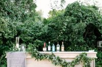 a simple and cool wedding drink bar of a white bar stand, with a greenery garland, a grey fabric menu is a lovely idea