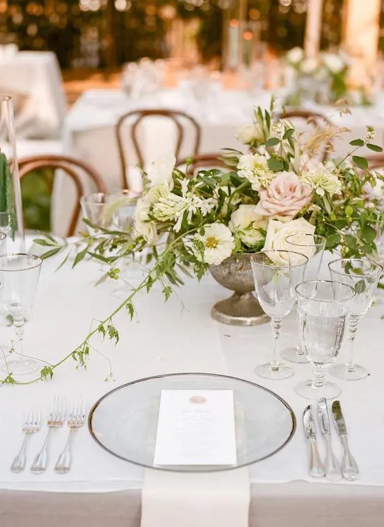 a sophisticated garden wedding tablescape with neutral linens, sheer plates, silver cutlery and a cool neutral and pink floral centerpiece
