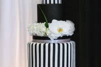 a sophisticated wedding cake with black and white vertical stripe tiers and a black one, with fresh white blooms and greenery