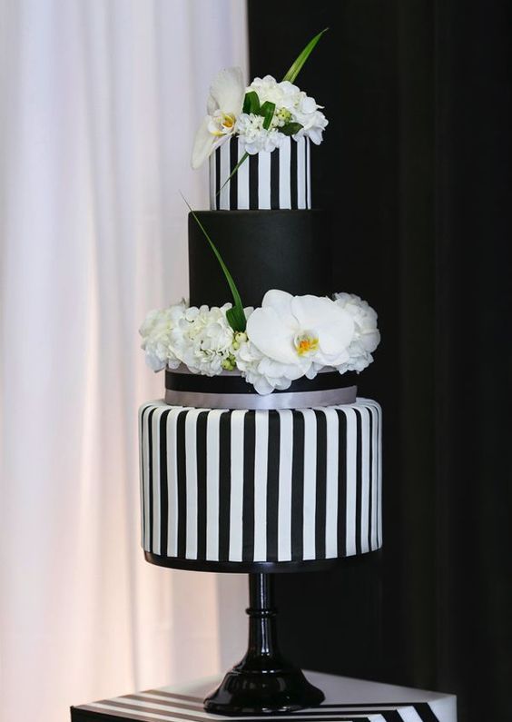a sophisticated wedding cake with black and white vertical stripe tiers and a black one, with fresh white blooms and greenery