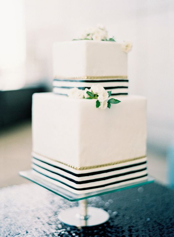 a square wedding cake with black and gold stripes, white blooms and greenery is a stylish idea for a modern wedding
