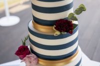 a striped navy and white wedding cake with gold stripes, pink, burgundy and fuchsia blooms and greenery for a summer wedding
