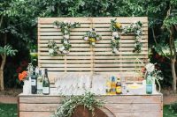 a stylish and rustic wedding drink bar of wooden planks, with greenery and bloom monograms and a greenery arrangement is a veyr chic and cool idea