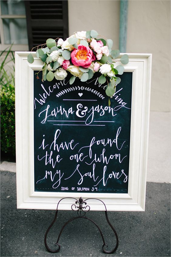 a stylish chalkboard sign in a white frame with calligraphy and pink and neutral blooms and greenery is a lovely idea for a vintage wedding