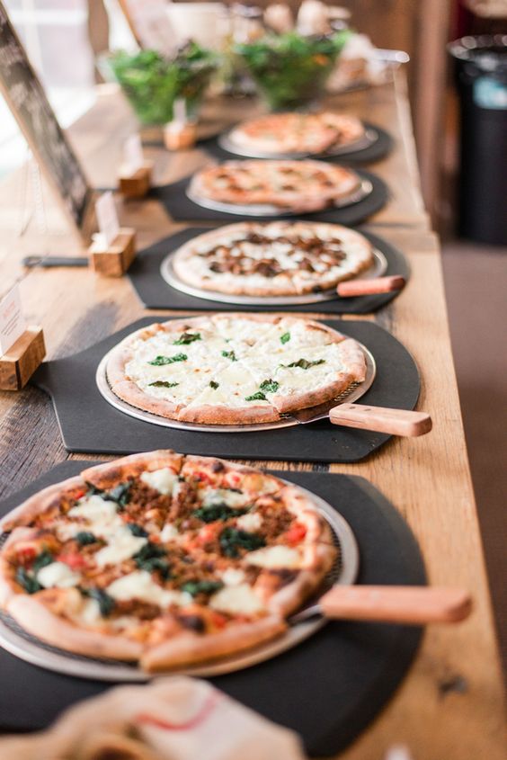 a stylish modern meets rustic pizza bar with pizzas on trays and on elegant black boards, marks on stands and a sign with the menu