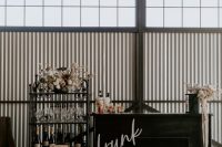 a stylish modern wedding bar of a black drink stand, a vintage metal shelving unit with neutral blooms is a lovely idea to rock
