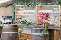 a stylish rustic wedding bar of barrels with a tabletop, bold blooms and greenery, wooden open shelves and a table is cool