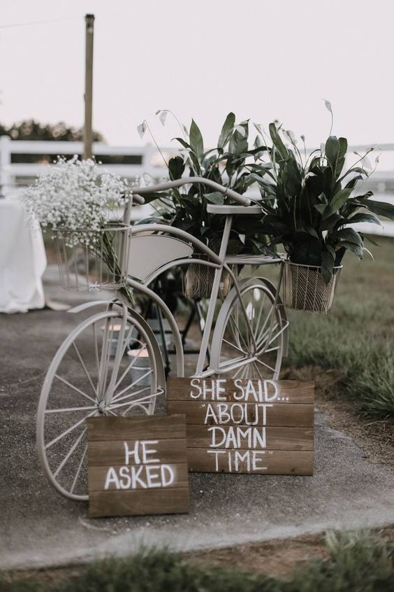 a stylish white bike with plaque signs, baby's breath and greenery in baskets is a lovely decor idea for a relaxed wedding