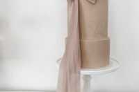 a taupe wedding cake with fun calligraphy and a large ribbon bow that matches in color is a fantastic and chic idea for a modern and trendy wedding