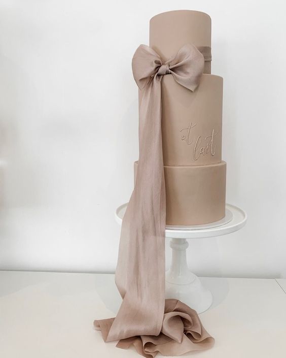 a taupe wedding cake with fun calligraphy and a large ribbon bow that matches in color is a fantastic and chic idea for a modern and trendy wedding