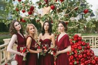 a unique wedding altar – an apple tree with red apples and piles of them on the floor, bridesmaids wearing mismatching burgundy maxi dresses
