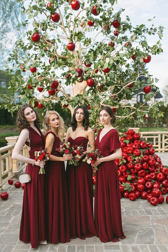 a unique wedding altar - an apple tree with red apples and piles of them on the floor, bridesmaids wearing mismatching burgundy maxi dresses