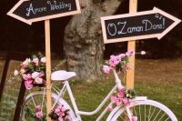 a white bike decorated with pink blooms, with crates with white blooms, chalkboard signs and a candle lantern