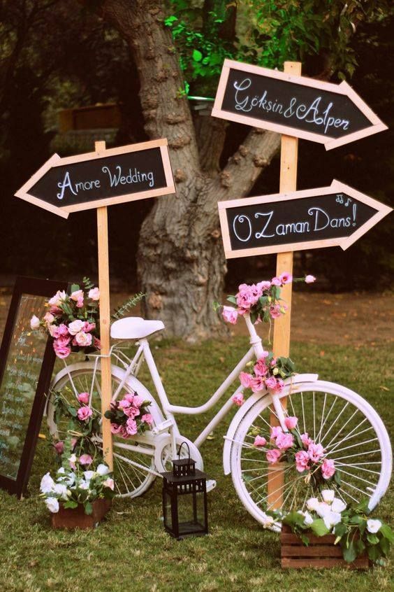 a white bike decorated with pink blooms, with crates with white blooms, chalkboard signs and a candle lantern
