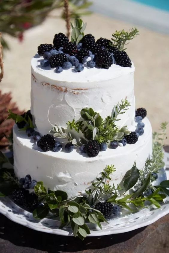 a white textural wedding cake decorated with greenery, blackberries and blueberires will fit many weddings