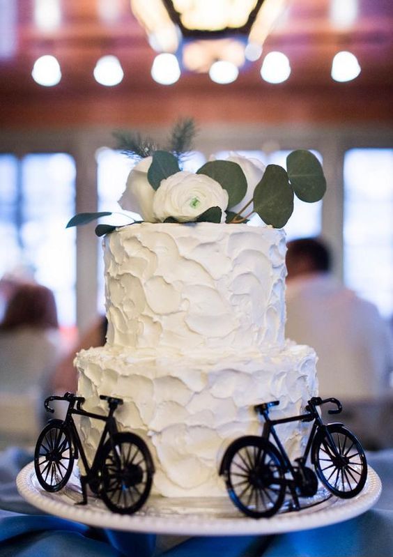 a white textural wedding cake topped with white blooms and greenery and decorated with black bikes is a lovely idea for a wedding