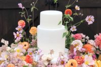 a white wedding cake surrounded with lush orange, yellow and lilac blooms and greenery all over are great for a garden wedding