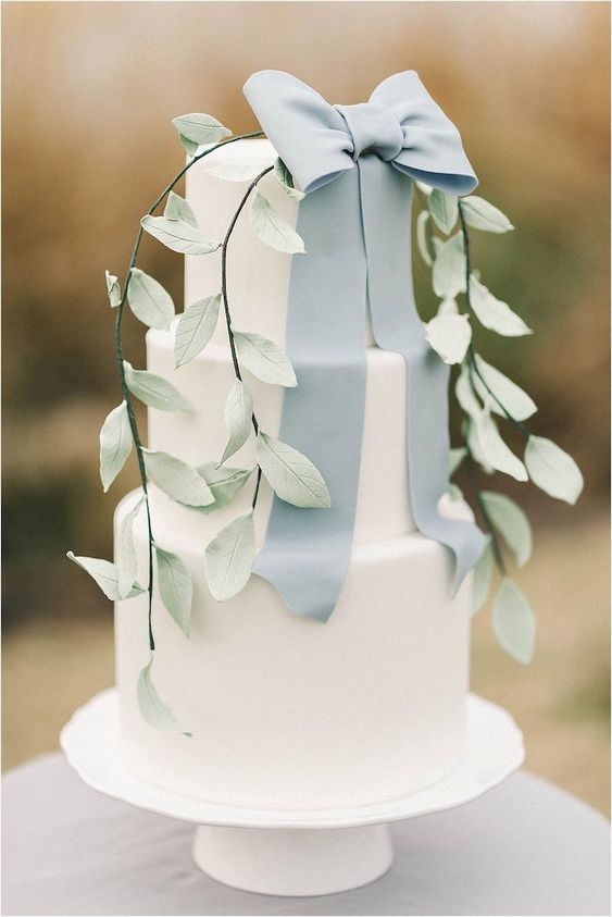 a white wedding cake with a sugar dusty blue ribbon bow and sugar leaves for a spring or summer wedding