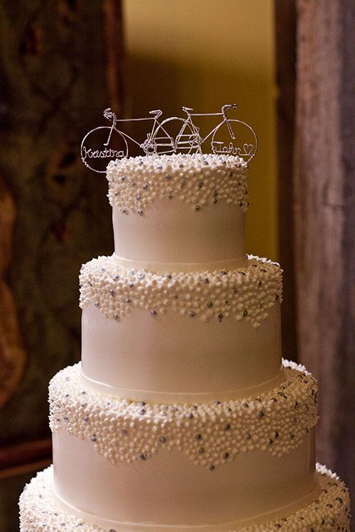 a white wedding cake with beads and two wire bike toppers is a stylish and chic idea for a modern wedding