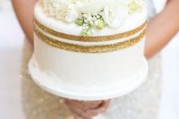 a white wedding cake with gold glitter stripes and white blooms is a chic and elegant idea for any modern wedding with a touch of glitter