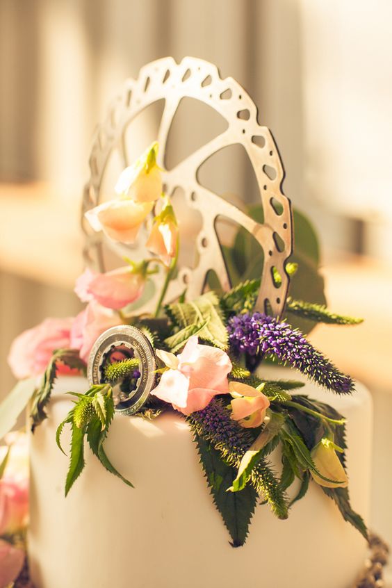 a white wedding cake with greenery, pastel blooms and a metal wheel and a large plywood one is a stylish idea for a wedding
