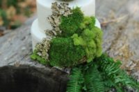 a wild woodland wedding cake in white decorated with moss, bark, leaves and a a faux nest with eggs on top