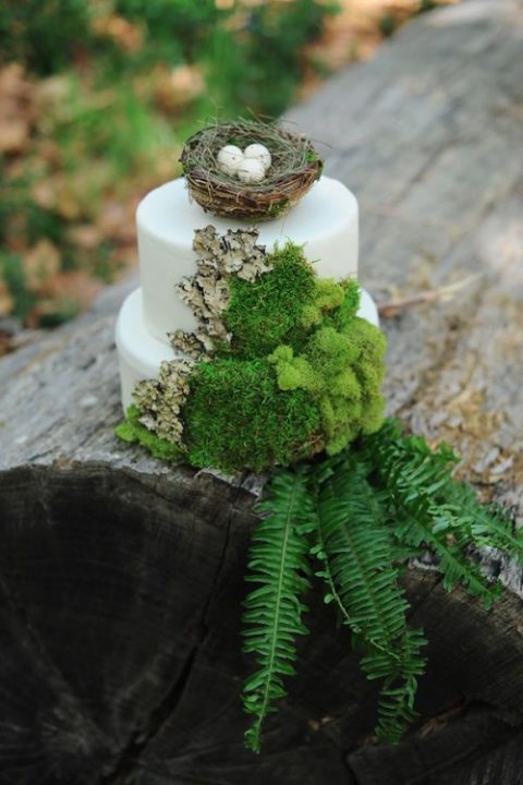 a wild woodland wedding cake in white decorated with moss, bark, leaves and a a faux nest with eggs on top