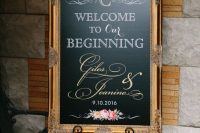 an elegant chalkboard sign in a very refined and beautiful gilded frame with floral arrangements, greenery and feathers