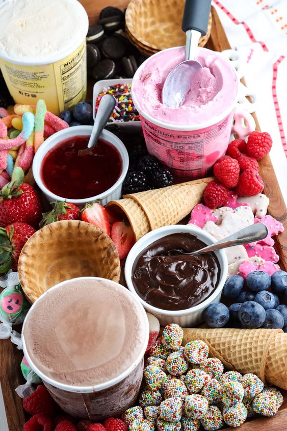 an ice cream board with candies, berries, cookies, ice cream, waffle cups and cones and various toppings is amazing