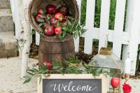 elegant fall wedding decor with wooden baskets with apples and greenery, a chalkboard sign, a candle lantern and an apple on a stand