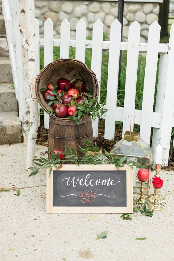 elegant fall wedding decor with wooden baskets with apples and greenery, a chalkboard sign, a candle lantern and an apple on a stand