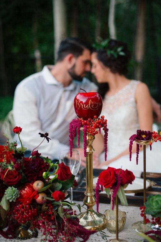 exquisite jewel-toned fall wedding decor with red blooms, berries, greenery and apples, a tall gold stand with berries and an apple with callgiraphy