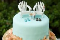a beach tiffany blue wedding cake with loungers, flipflops, a bucket with seashells and seashells and sand around