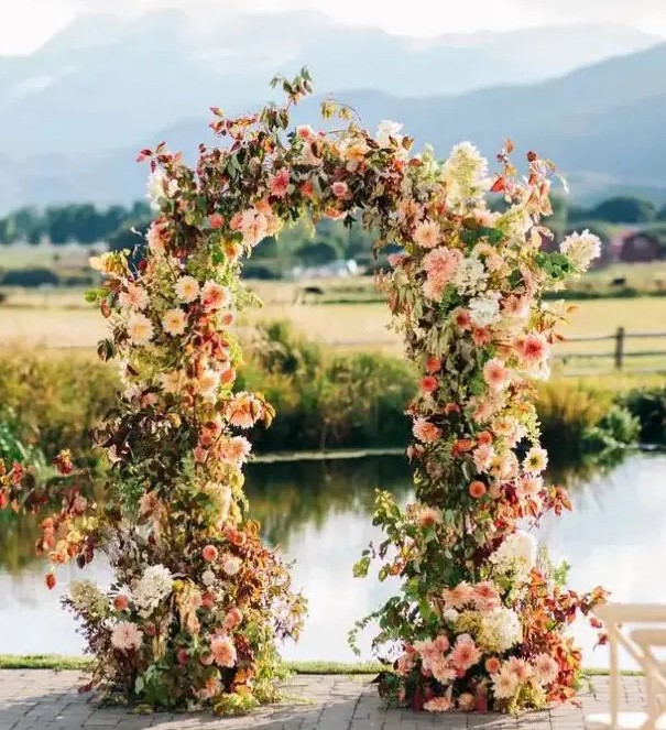 a beautiful and bright fall wedding arch of pink, blush and neutral blooms, including dahlias and hydrangeas, greenery and bold foliage is a very cool and cheerful idea
