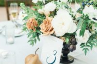 a beautiful and simple wedding centerpiece of white and rust-colored blooms, greenery and grapes, pears and a table number
