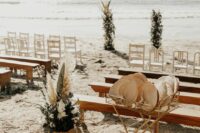 a beautiful beach wedding ceremony space with white chairs and stained benches, white blooms, greenery and pampas grass
