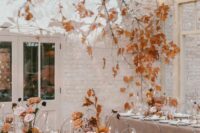 a beautiful neutral fall wedding reception space with a branch with fall leaves over it and floral and leaf arrangements on the tables, neutral candles