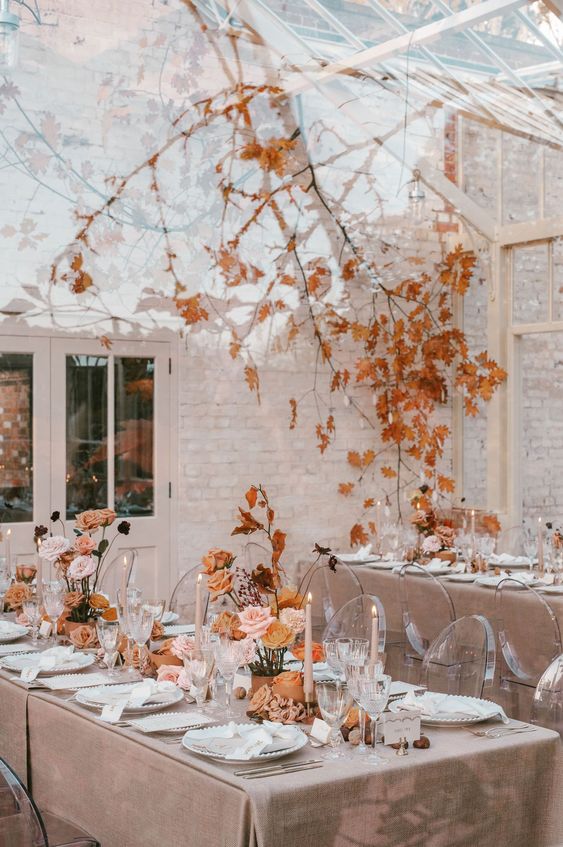 a beautiful neutral fall wedding reception space with a branch with fall leaves over it and floral and leaf arrangements on the tables, neutral candles