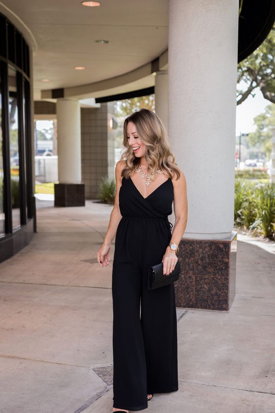 a black spaghetti strap jumpsuit with wideleg pants, a black clutch and a statement necklace