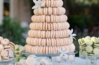 a blush macaron tower with pastel blue blooms is a very cool idea, serve more pastel macarons to make the dessert table evenmore tender